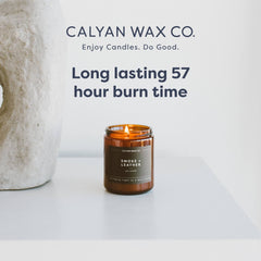 Amber glass jar of Calyan Wax Co candle on a table in cozy setting.