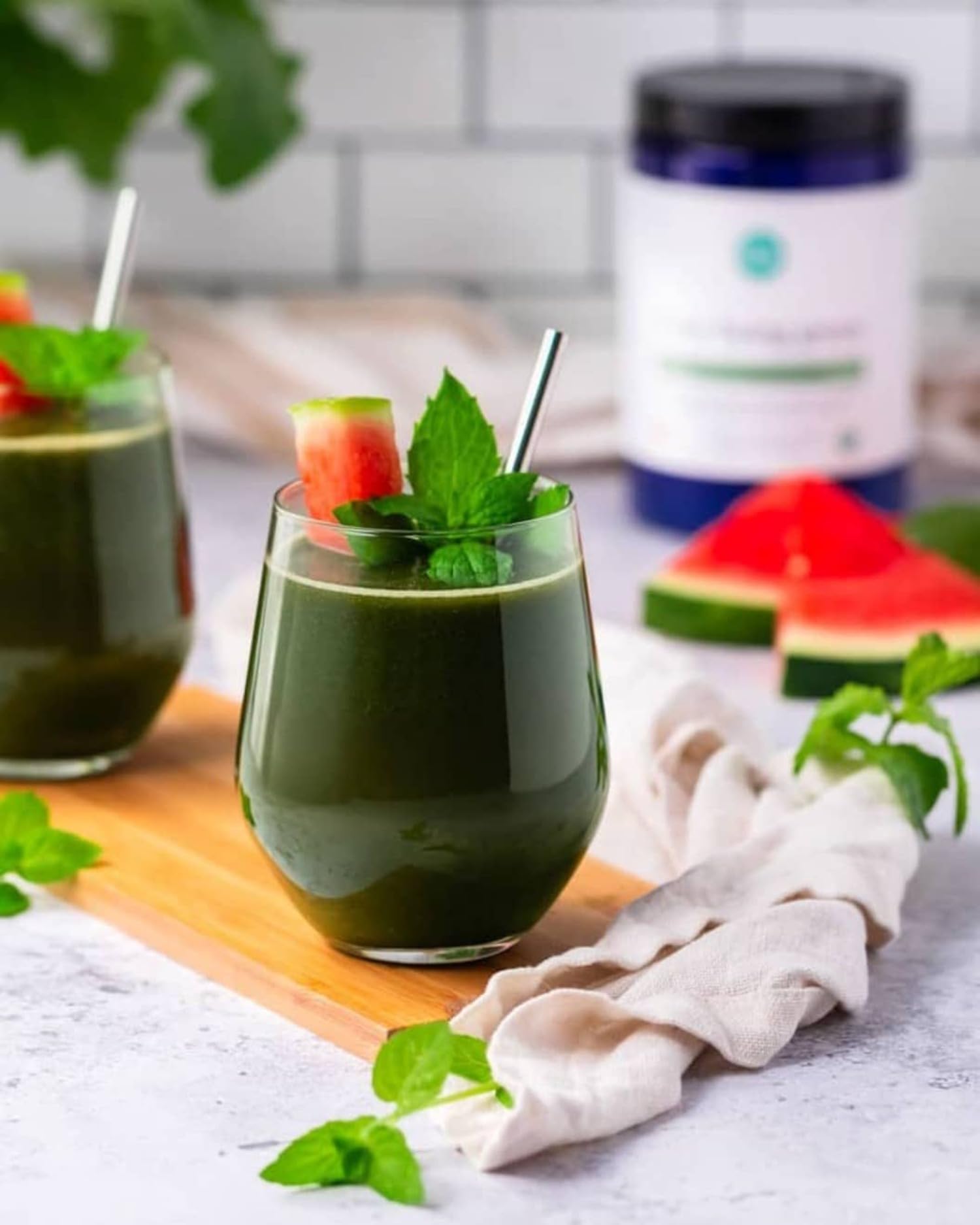 Pouring Ora Organic Greens Powder into a glass of water with fruit garnish.