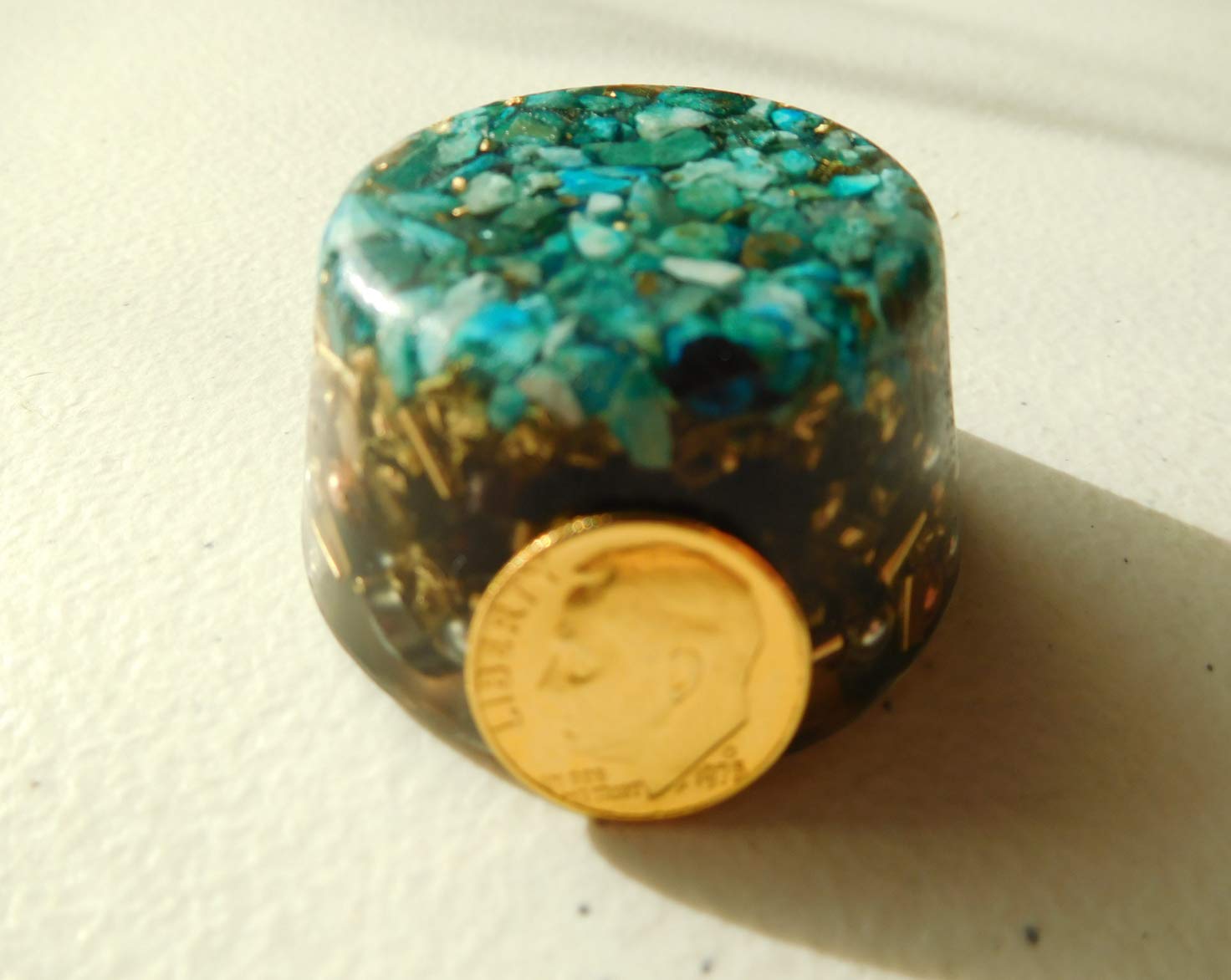 Turquoise Single Crystal Tower Buster Orgone Generator on display beside plants.